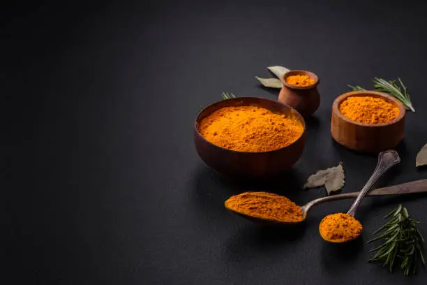 Bright yellow turmeric or curry spice for Asian food preparation on dark concrete background