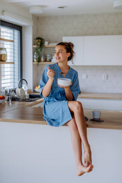 jeune femme prenant du muesli pour le petit-déjeuner dans sa cuisine, la routine matinale et le concept de mode de vie sain. - oatmeal breakfast healthy eating food photos et images de collection