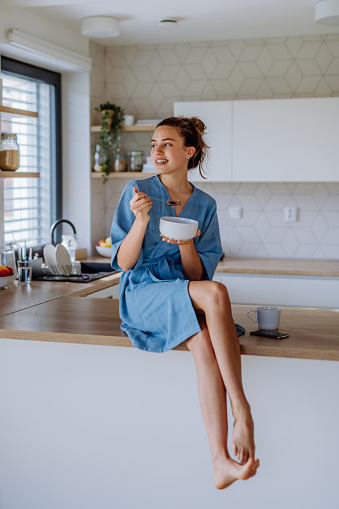Young woman having a muesli for breakfast in her kitchen, morning routine and healthy lifestyle concept.