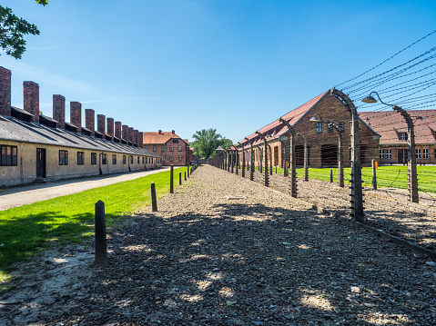 Oświęcim, Poland - June 05, 2019: Electric fence with barbed wire and brick prison buildings at the Auschwitz-Birkenau concentration camp in Oświęcim, Poland. Europe.