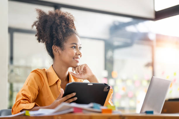 istock Confident ethnic businesswoman using tablet and laptop at work, thinking and looking away outside. 1460227100