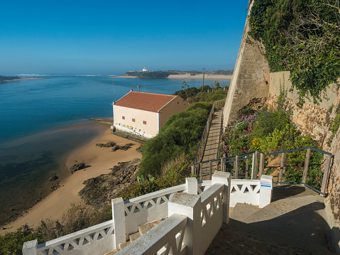 Idyllic view of the mouth of Mira river flowing into the Atlantic Ocean with stairs leading to port and ferry and small beach house. Vila Nova de Milfontes, Vicentine Coast Natural Park Portugal.