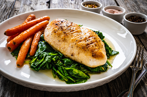 Fried chicken breast with spinach and carrots on wooden table