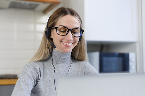 Portrait of smiling young female wearing headset with microphone to talk to clients on video call or web conference