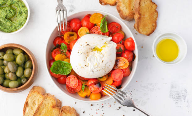 Farmer Italian soft cheese mozzarella di bufala campana served with fresh basil and red and yellow cherry tomatoes, croutons, homemade pesto, olives. Healthy Italian summer food, white background