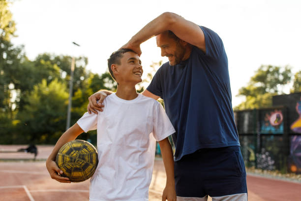 Proud father stroking his teenage son's hair and smiling at him after playing basketball together stock photo