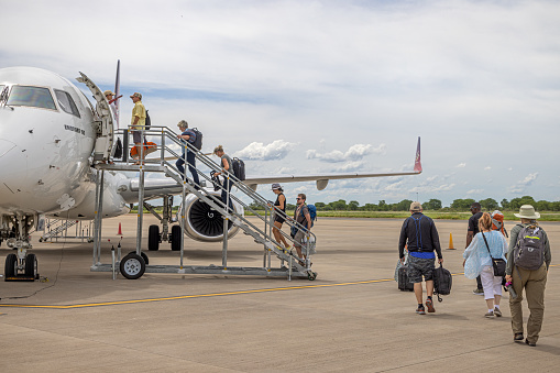 Maun International Airport, Botswana - December 19th 2022:  Passengers boarding a small jet aircraft, a Embraer190 ZS-YAY from FlyAirLink on the open tarmac in Maun Airport