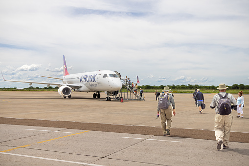 Maun International Airport, Botswana - December 19th 2022:  Passengers boarding a small jet aircraft, a Embraer190 ZS-YAY from FlyAirLink on the open tarmac in Maun Airport