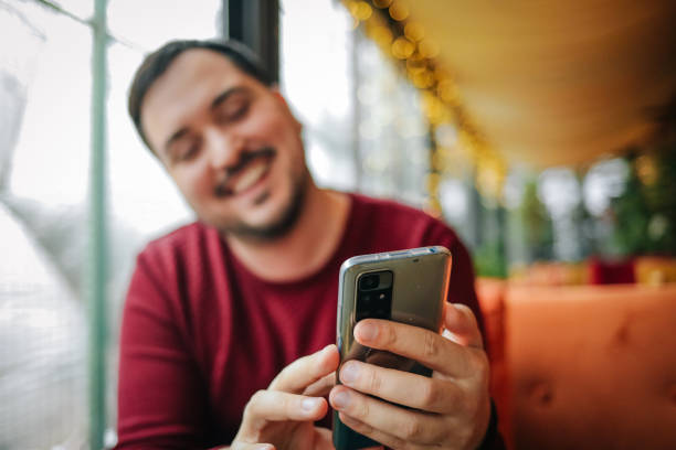 istock Young smiling man sitting in coffee shop and using phone 1460256354