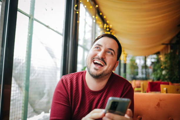 istock Young smiling man sitting in coffee shop and using phone 1460256448