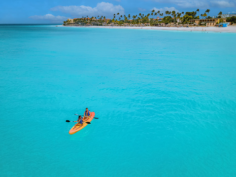 Couple Kayaking in the Ocean on Vacation Aruba Caribbean sea, man and woman mid age kayak in ocean blue clear water with white beach and palm trees Aruba