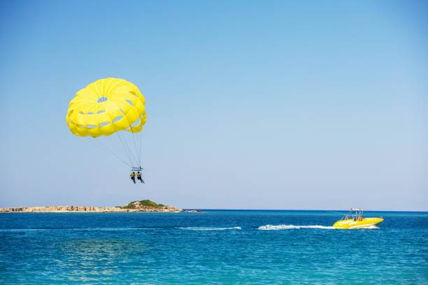 istock Parasailing above the ocean. Yellow parasail wing pulled by a boat. Sport activity on the beach. 1460258648