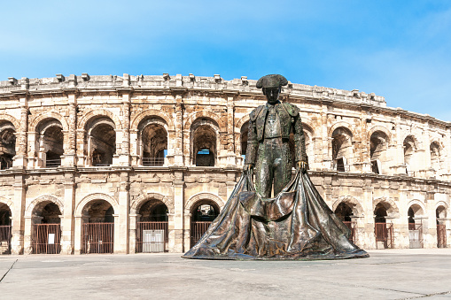 View on the roman amphitheatre, with a matador statue in foreground, in the centre of Nîmes city,  in France. October, 25, 2022.