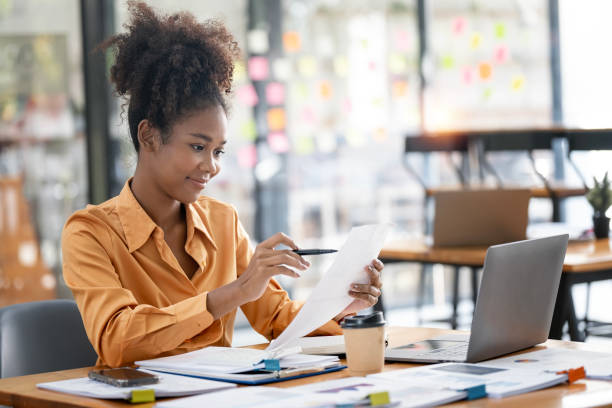 istock young afro american businesswoman working on paperwork and laptop computer at open workspace. 1460260111