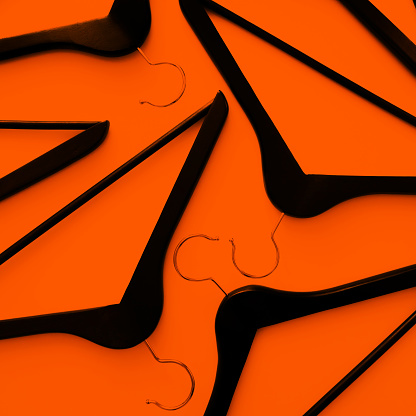 Black wooden clothes hangers on an orange background. Square image. Fashion and shopping concept.