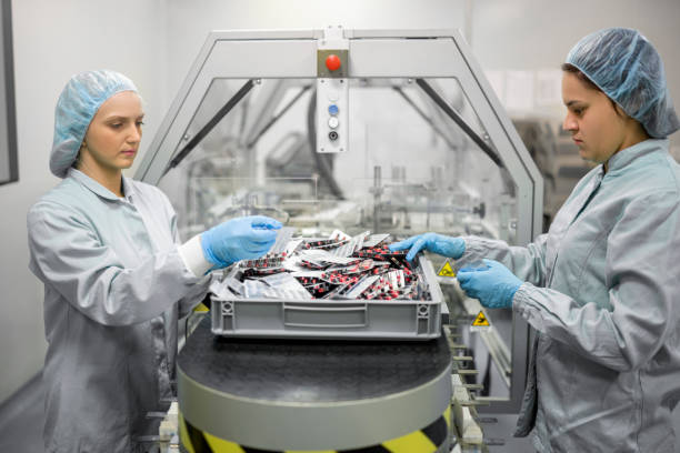 Pharmaceutical Industry Workers in Action Two skilled young female workers in protective gear demonstrate precision and focus as they operate a high-tech packaging machine, producing blister packs containing capsules in a state-of-the-art pharmaceutical production facility. drug manufacturing stock pictures, royalty-free photos & images