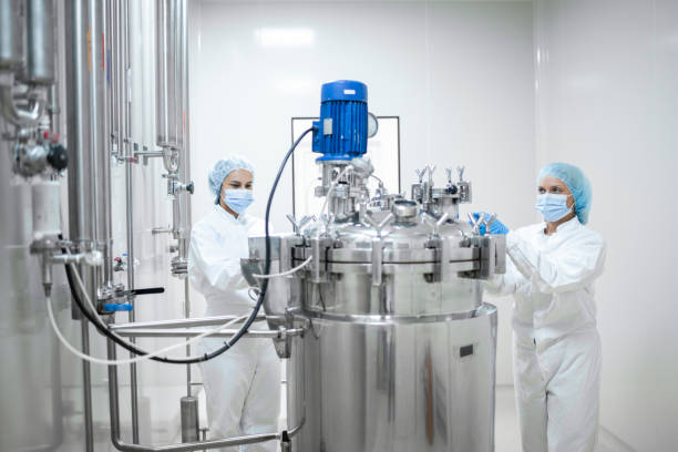 Production Process in Pharmaceutical Industry Two young female workers in protective gear operate a stainless steel tank and vessel in a pharmaceutical production facility. The tank is equipped with an agitator for precise mixing of substances, ensuring the smooth production of life-saving medications. The facility employs advanced technology and strict controls to maintain the sterility and efficacy of the drugs being produced. pharmaceutical factory stock pictures, royalty-free photos & images