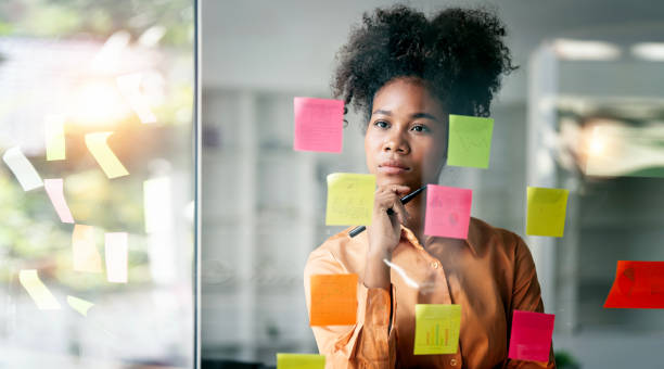 istock Young smiley attractive, businesswoman using sticky notes in glass wall to writing strategy business plan to development grow to success 1460262303
