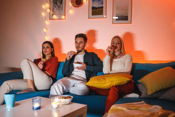 istock Three roommates snacking on cookies while watching a movie on a TV 1460265183
