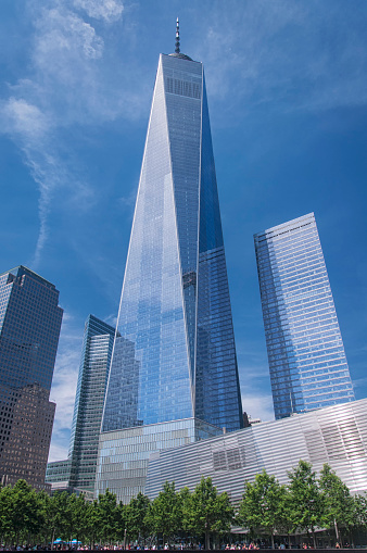 The freedom tower rising above the september 11th memorial in new york city, new york on a blue sky sunny day.