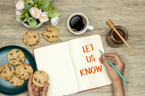 let us know concept on notebook, hand holding a pencil an cookies, cup coffee with homemade chocolate chip cookies with honey jar on wood table