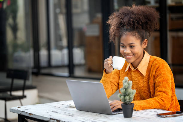istock Attractive african young confident woman holding coffee cup and using laptop computer, sitting at open co-workspace. 1460270241