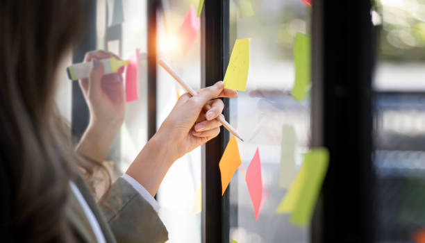 istock Team or staff discussing with sticky notes a schedule on glass wall for future project together, innovation and vision business meeting in a modern office 1460271807