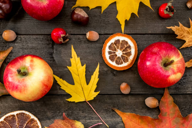 Autumn background maple leaves, apples, rose hips, nuts, chestnuts, dried oranges on a wooden table