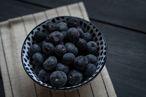 Fresh ripe garden blueberries in a wicker bowl on dark rustic wooden table. with copy space for your text