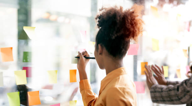 istock Young businesswoman creative team using post it notes in glass wall to writing strategy business plan to development grow to success. 1460277495