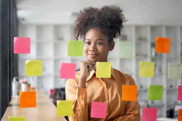 istock Young smiley attractive, businesswoman using sticky notes in glass wall to writing strategy business plan to development grow to success 1460277743