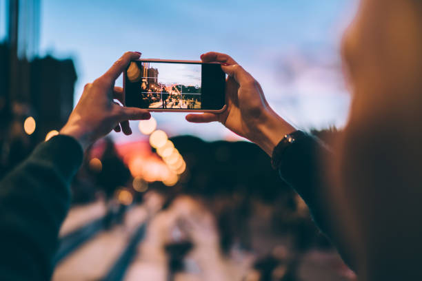 istock Selective focus on modern cellular phone using for clicking pictures via camera, millennial woman tourist taking photos or shooting video via mobile phone during evening walk for exploring new city 1460278954