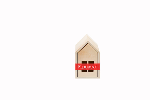 Model house made of wood with red tape and Repossessed message on a plain white background. Rising mortgage interest rates concept.