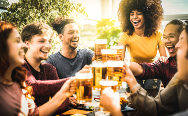 Multiracial friends drinking and toasting beer pint at brewery bar restaurant - Beverage life style concept with guy and girl having fun together at brew garden - Warm filter with focus on right woman stock photo