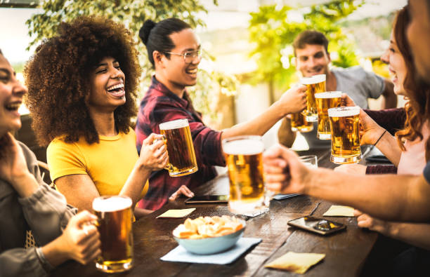 Multicultural people drinking and toasting beer pint at brewery bar restaurant - Beverage life style concept with guy and girl having fun together at brew garden - Warm filter with focus on left woman stock photo