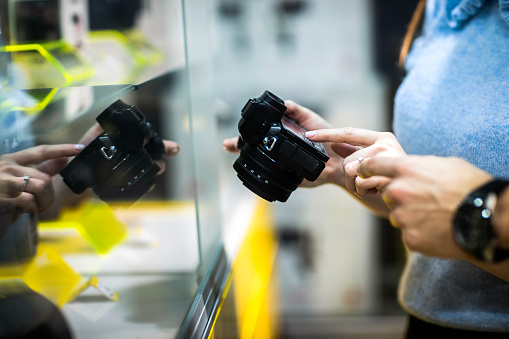 Close up on female's hands seen holding photo camera while salesman is helping her with the selection in a camera shop.