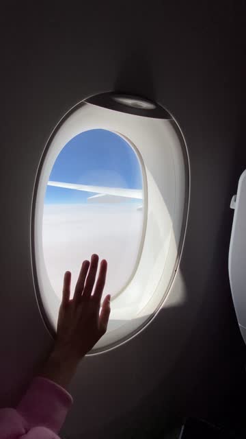 Point of view woman's hand touching airplane window, looking at the sky