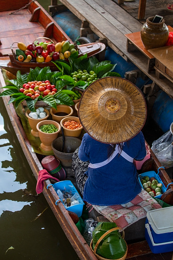 Thai woman in straw hat selling food on boat at floating market in Thailand