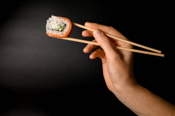 istock Philadelphia roll in hand holding with bamboo chopsticks on dark background. 1460294229