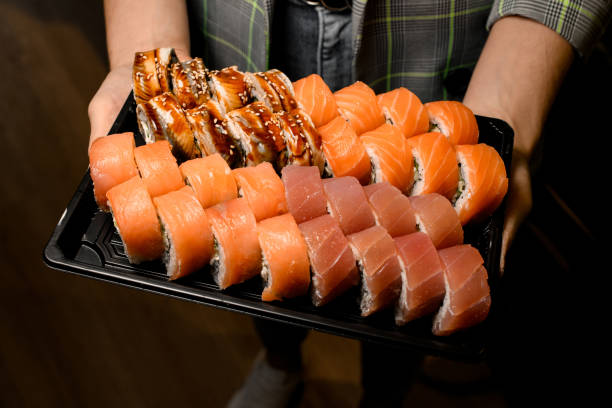 Sushi sets - philadelphia with salmon, tuna, eel in black box in male hands. Top view.