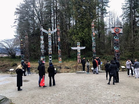 Vancouver, British Columbia, Canada - January 1st, 2023: A group of tourists admire the totem poles in Stanley Park on a chilly New Years day in Vancouver, Canada.