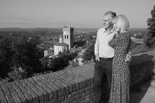 Monochrome image of a senior couple on vacation admiring the Tuscan countryside at the village of San Miniato, Italy. The image has grain.