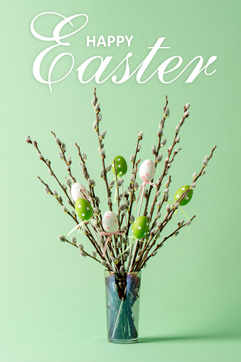 Easter eggs decorations and pussy willow twigs with catkins in a vase. Happy Easter lettering.
