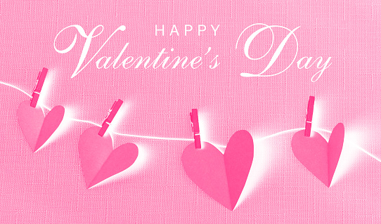 Pink paper cut hearts hanging on a clothesline with wooden clothespins. HAPPY VALENTINE'S DAY text is in the center. Negative image effect. Can be used as a design for Valentine's day holiday greeting cards or posters.