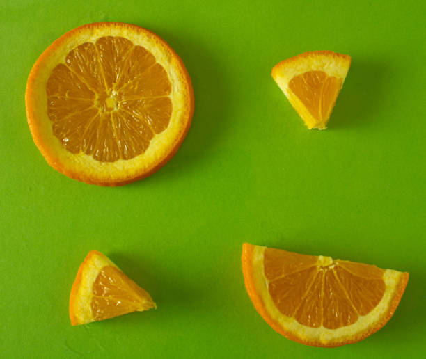 istock An orange cut into different shapes, a circle, a semicircle and a triangle form an abstract whole on a green surface 1460303996