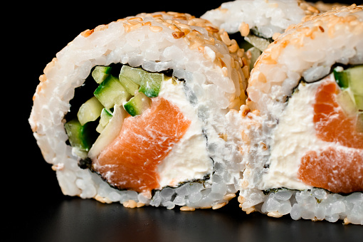 selective focus on the filling of sushi rolls california with smoked salmon, cream cheese, cucumber, sesame seeds on dark background.