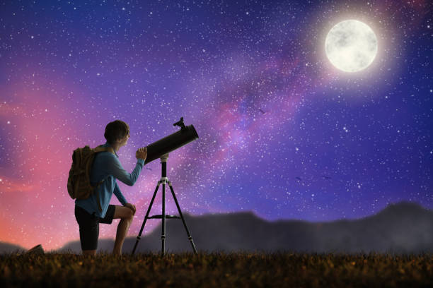 Young man looking at stars through telescope. Camping and hiking fun. Outdoor astronomy hobby. Teenager watching night sky with milky way. Teen observing planets and moon. Nature exploration.