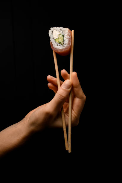 istock male hand gently holding Philadelphia roll with bamboo chopsticks on dark background. 1460306837