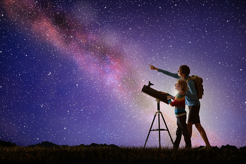 Man and child looking at stars through telescope. Family camping and hiking fun. Outdoor astronomy hobby. Parent and kid watch night sky with milky way. Boy observing planets and moon.