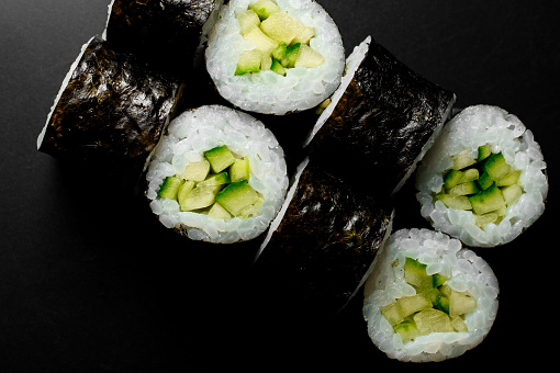 Close-up top view on classic vegetarian kappa maki sushi rolls with fresh cucumbers and rice wrapped in nori on dark background
